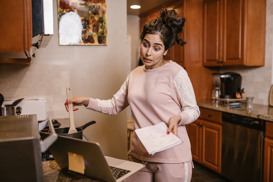 Woman multitasking in her kitchen with a laptop and notebook, cooking and working from home
